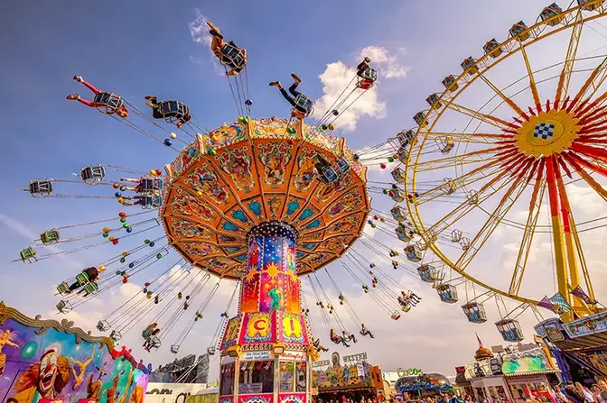 Manège de chaises volantes et grande roue sous un ciel bleu